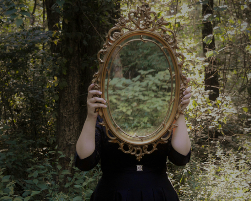 Person holding a decorative mirror in a forest setting