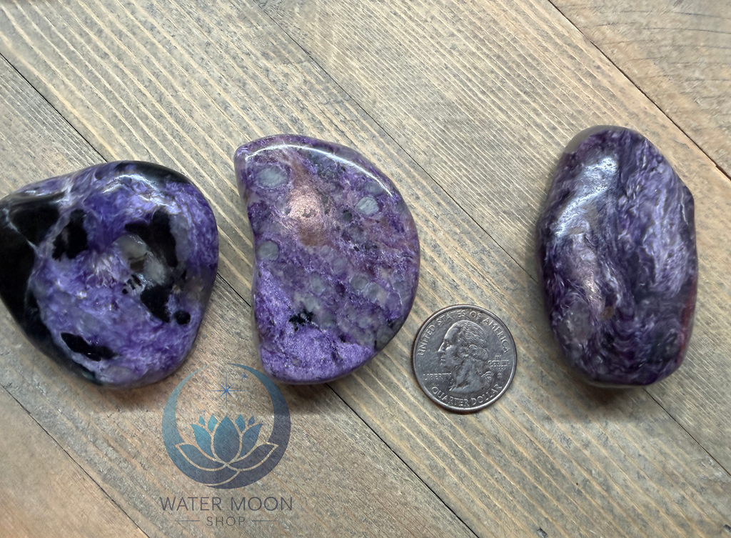 Three purple stones on a wooden surface with a quarter for scale, featuring the Water Moon Shop logo.