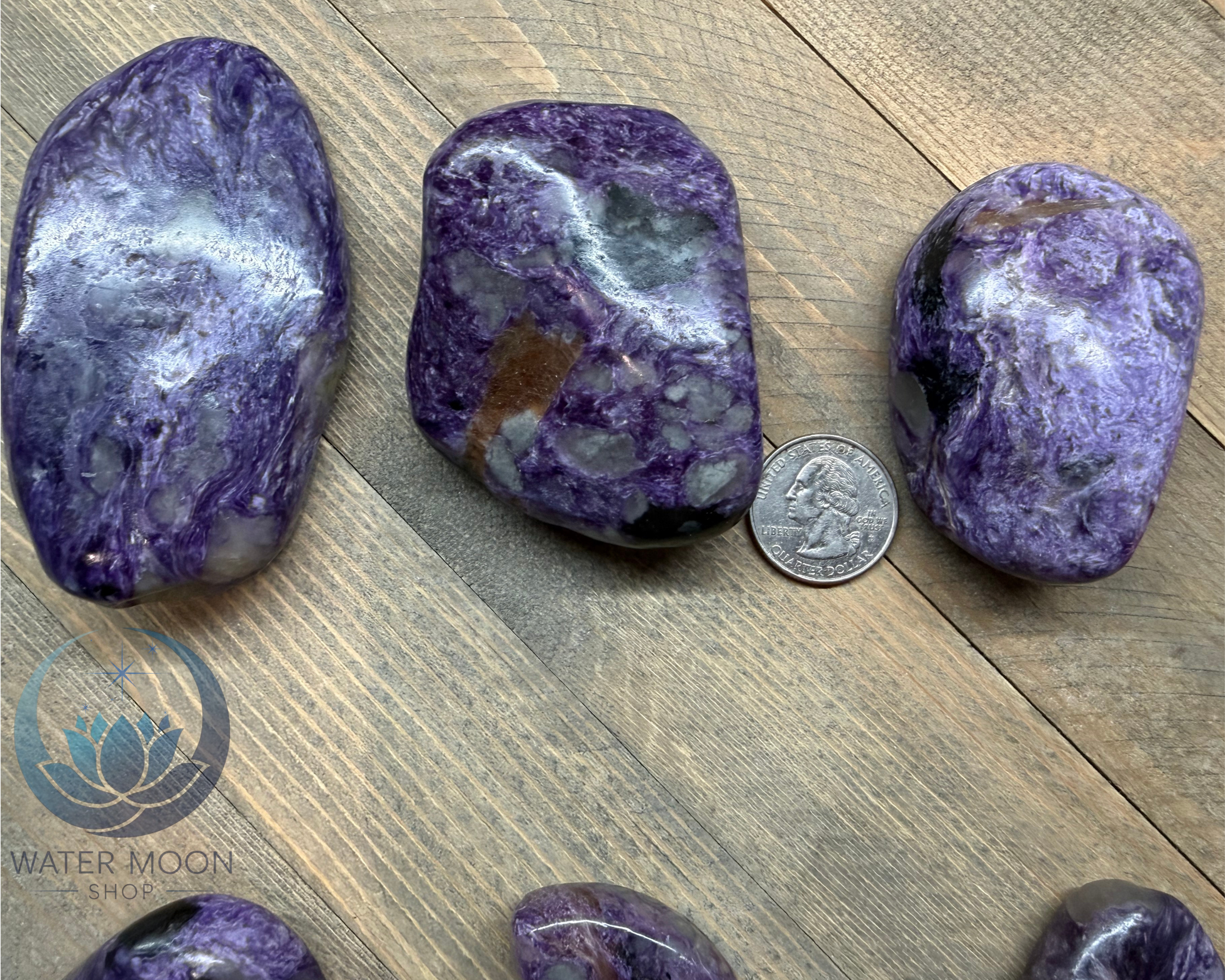 Three purple stones on a wooden surface with a coin for scale, featuring the Water Moon Shop logo.