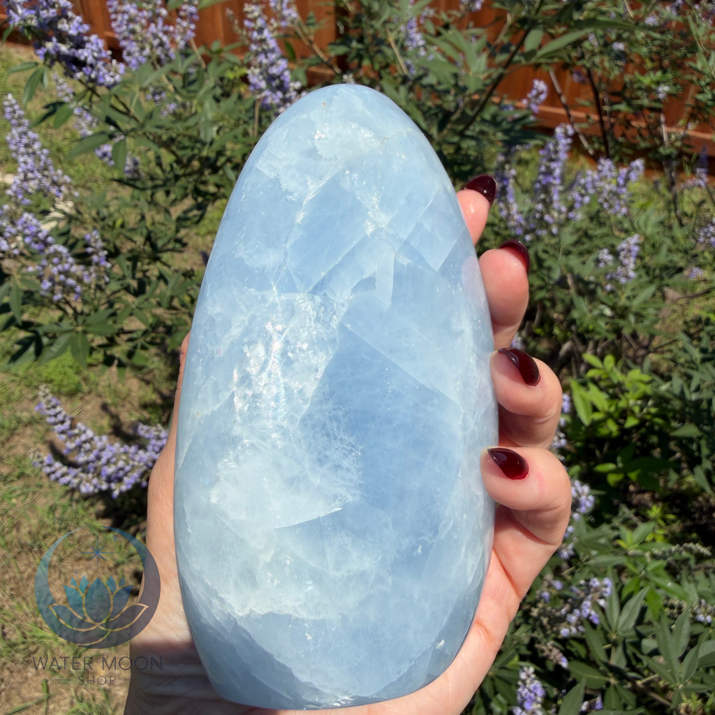 Hand holding a large blue crystal with a natural outdoor background