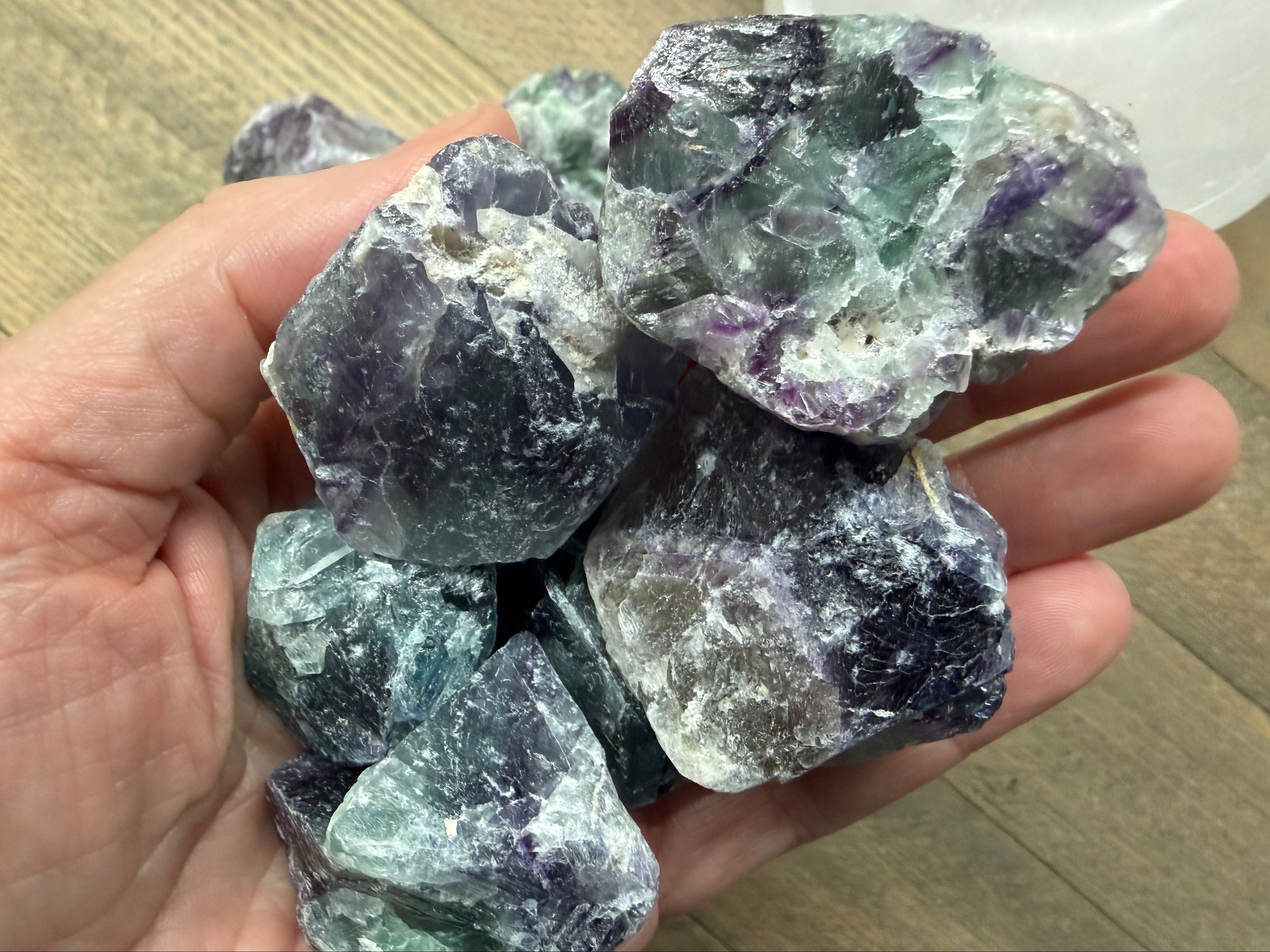 Hand holding a collection of purple and green crystals on a wooden surface