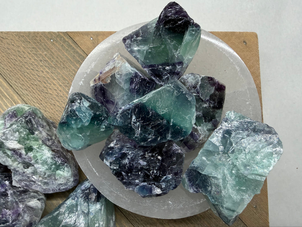 Collection of raw fluorite crystals on a white plate with a wooden surface underneath.