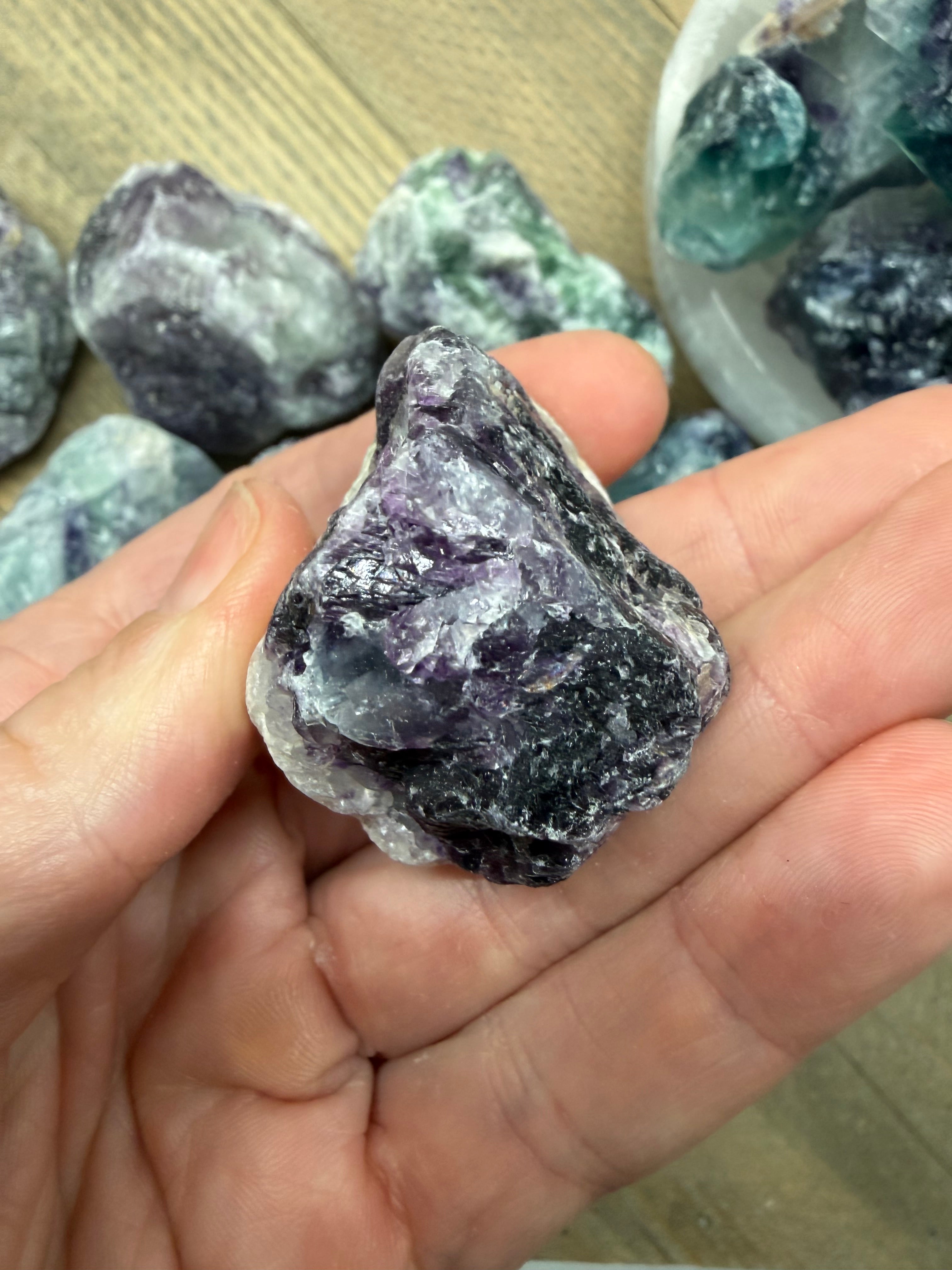 Hand holding a rough purple crystal with more crystals in the background