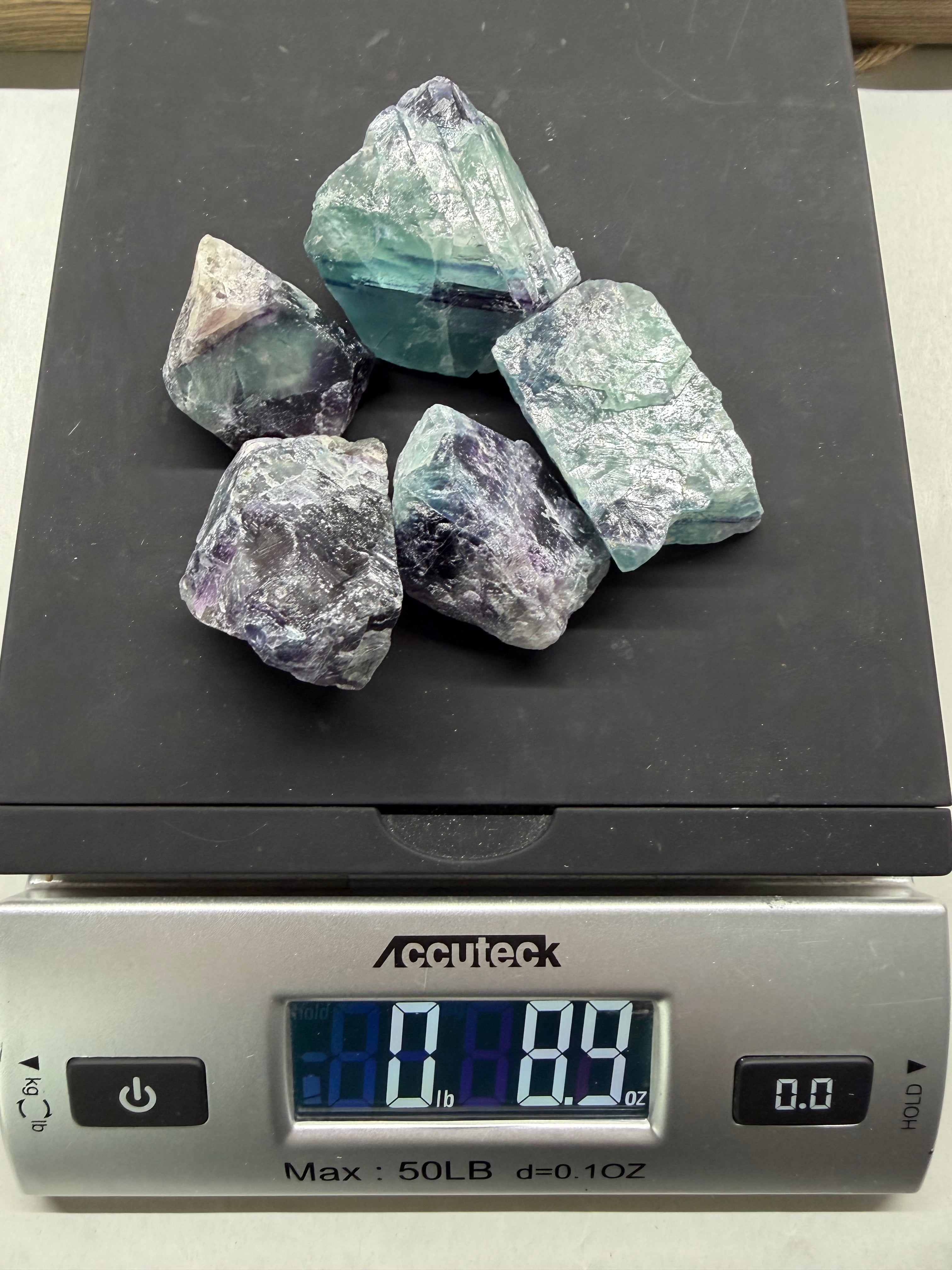 Raw gemstones on a digital scale with a visible weight reading.