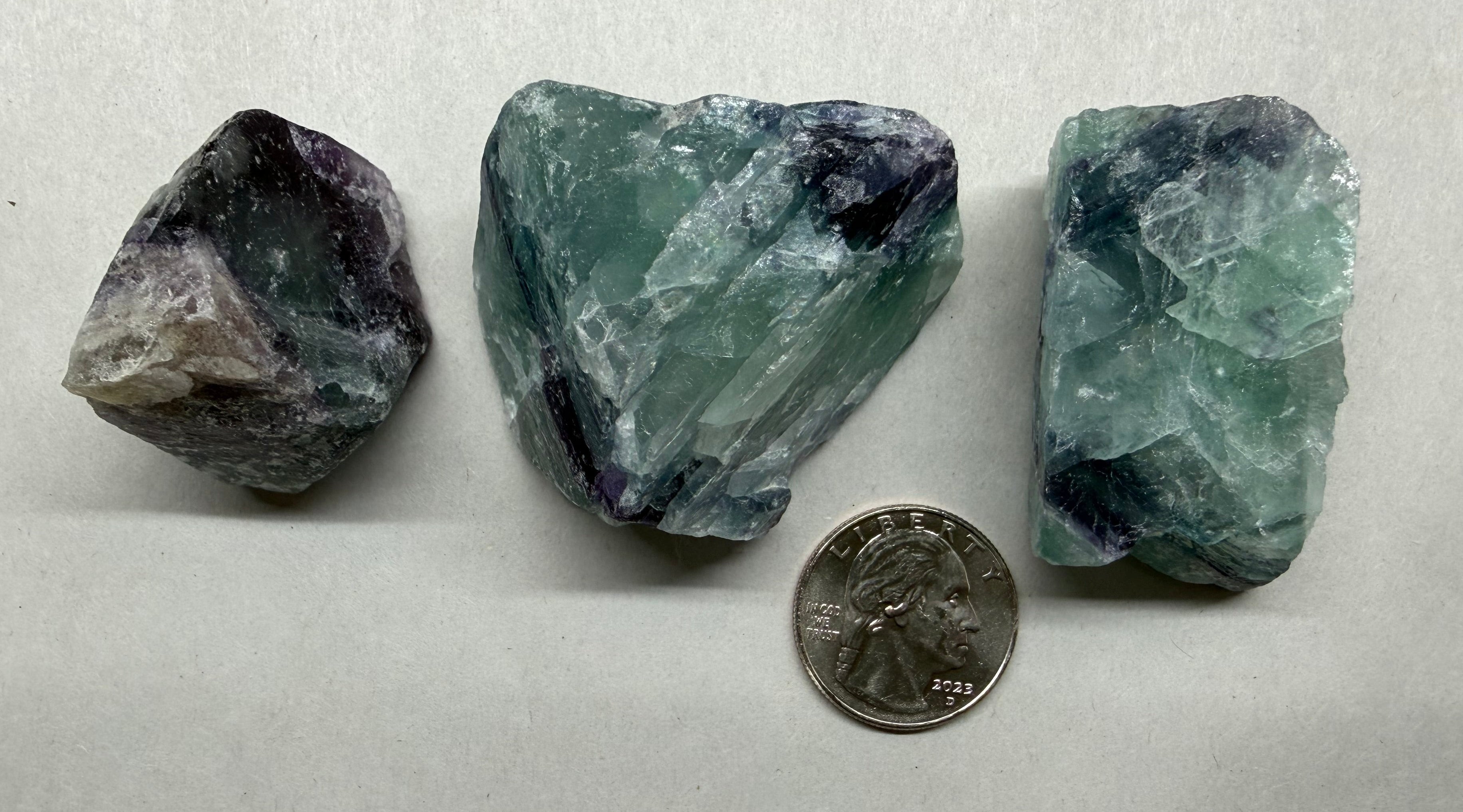 Three raw crystals on a white surface with a quarter for scale.