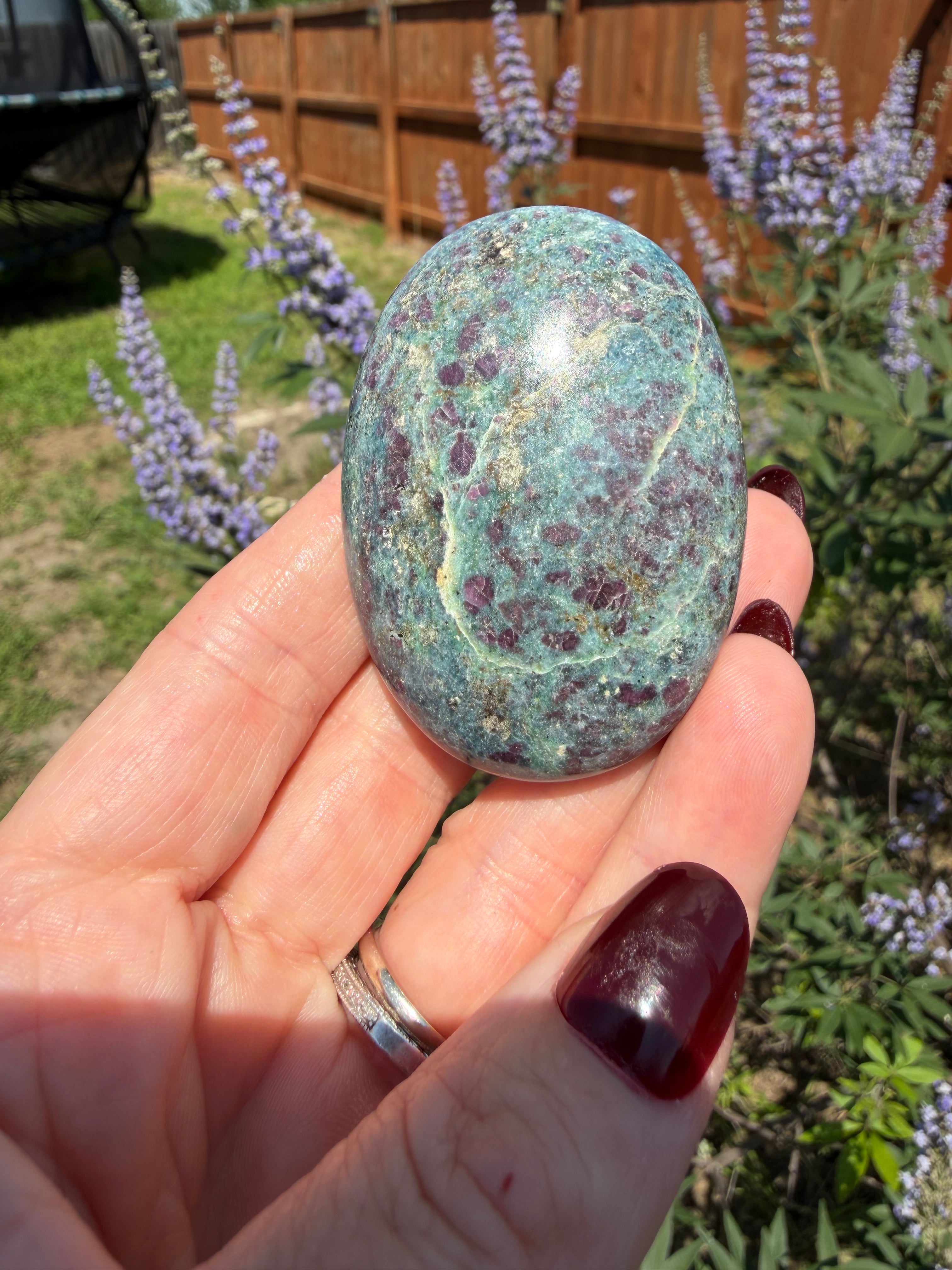 Hand holding a greenish-blue stone with purple markings, outdoors.