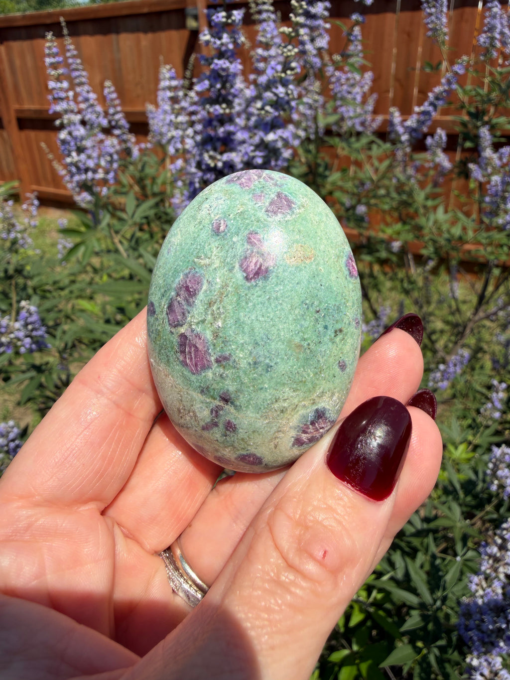 Hand holding a green and purple speckled egg with a garden background
