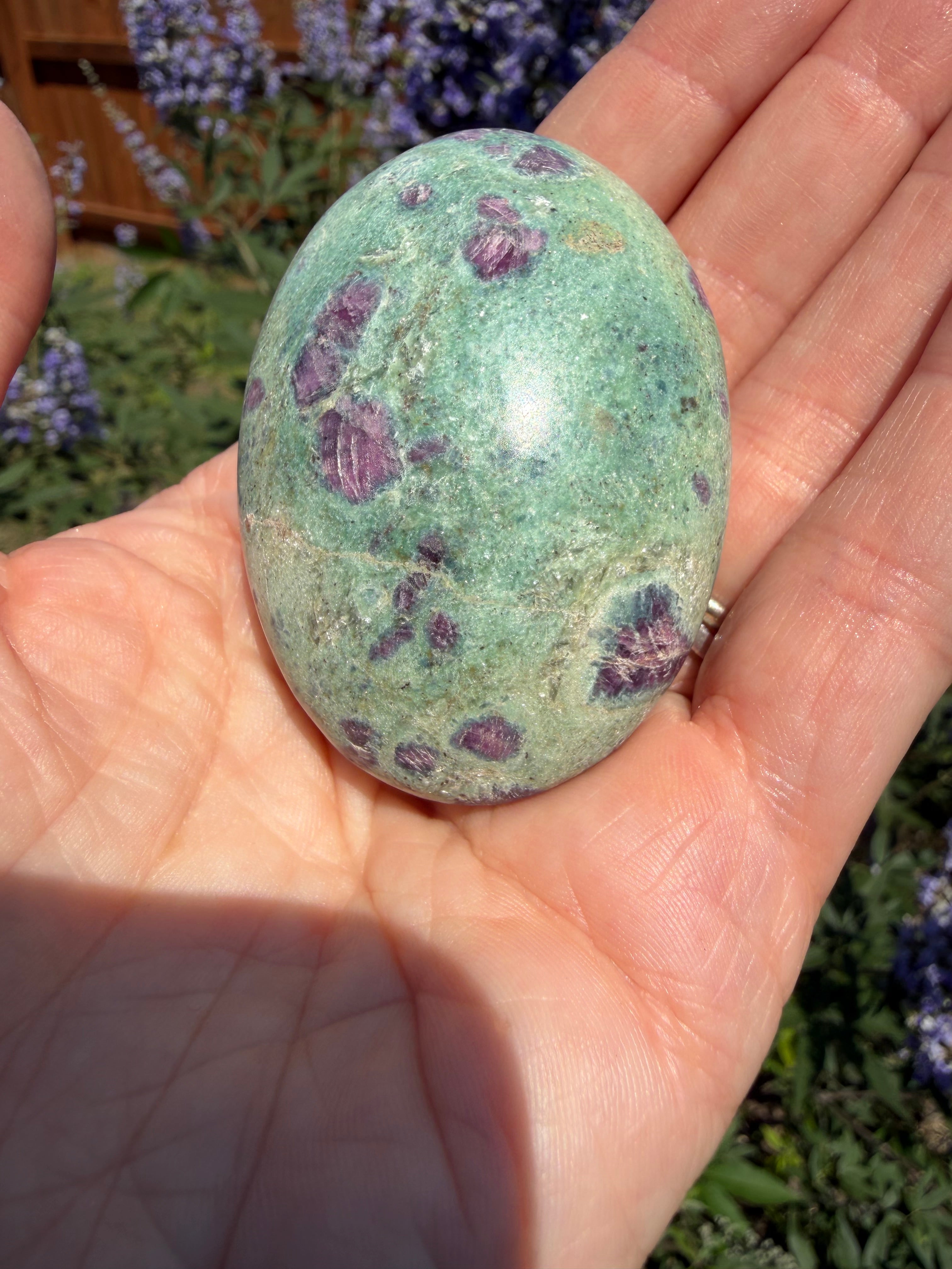 Hand holding a green stone with purple spots against a blurred natural background