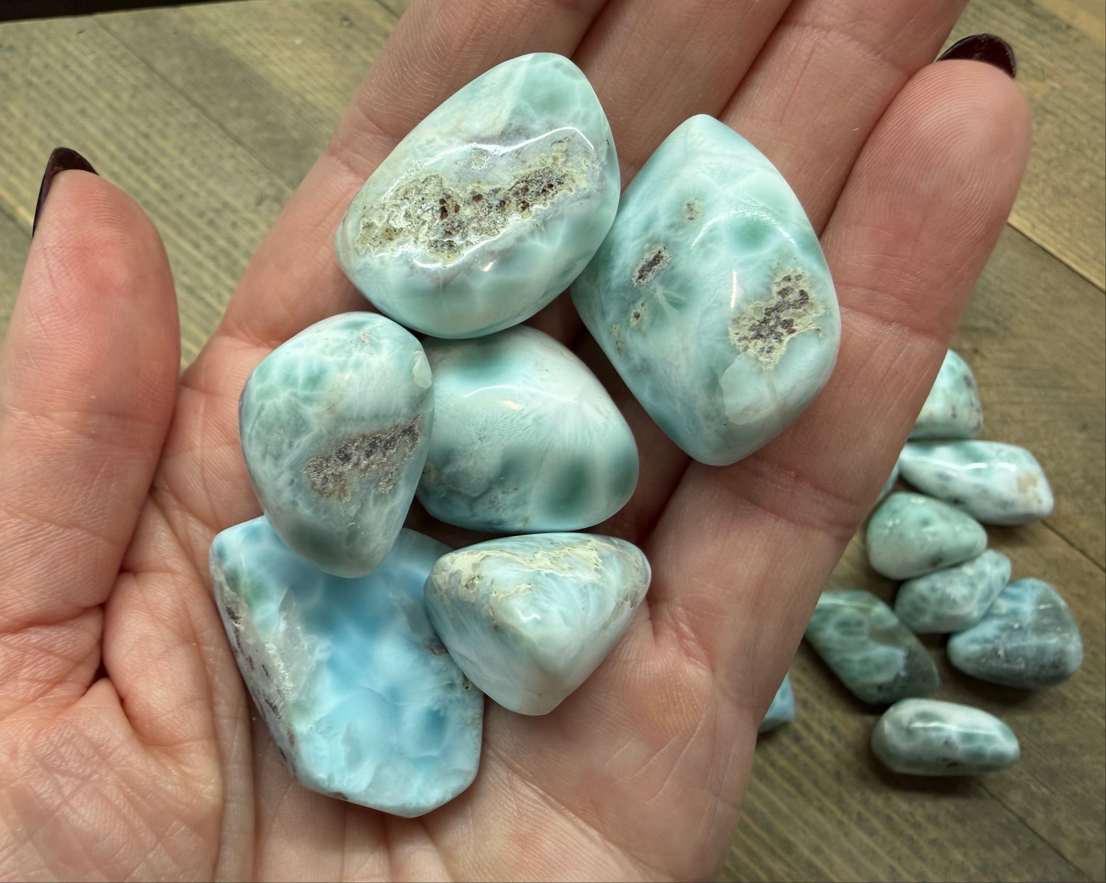 Hand holding several light blue-green larimar stones on a wooden surface.