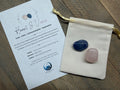 Two stones in a drawstring bag with an informational card on a wooden surface