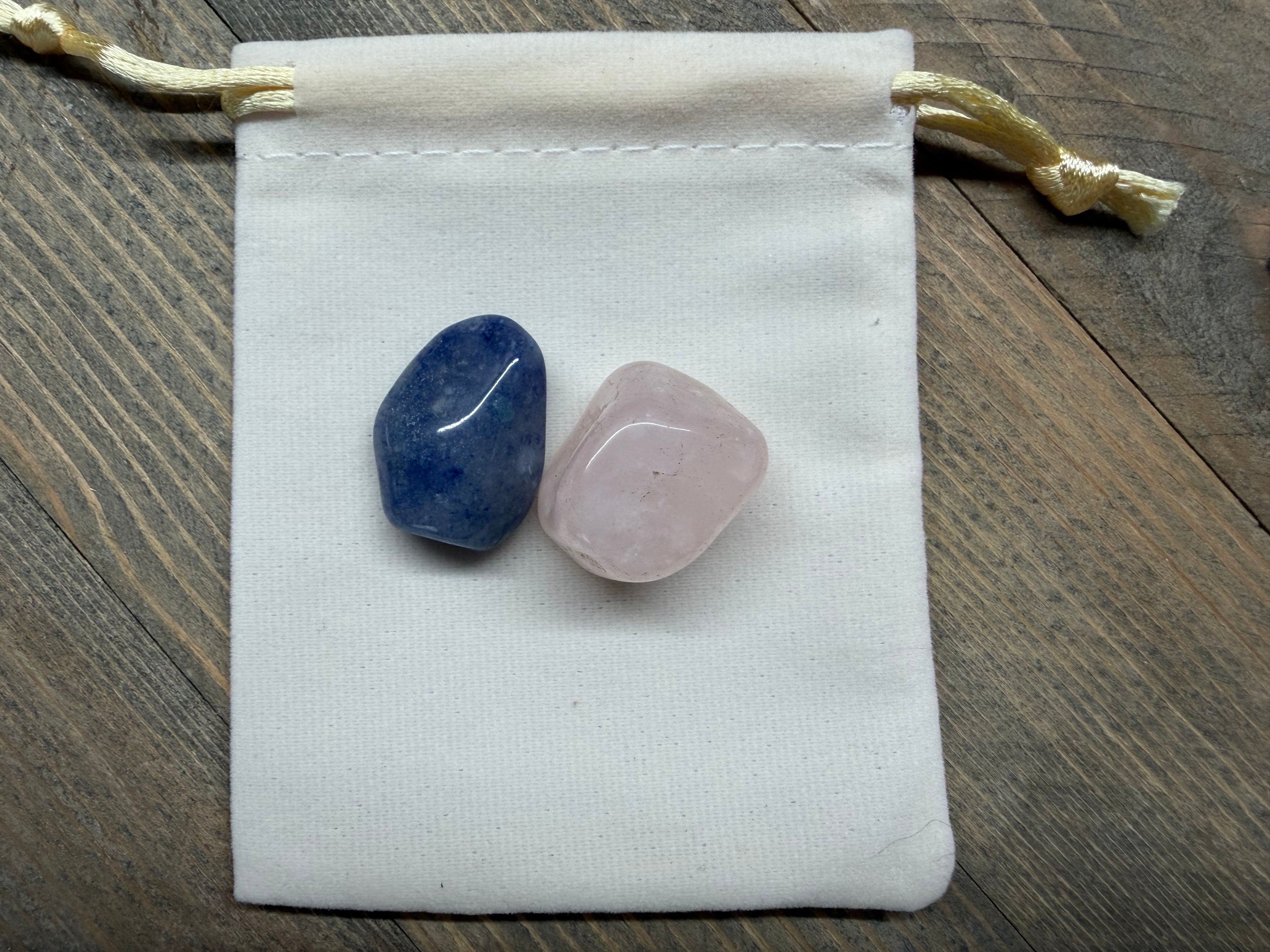 Two crystals, one blue and one pink, on a white drawstring bag against a wooden background.