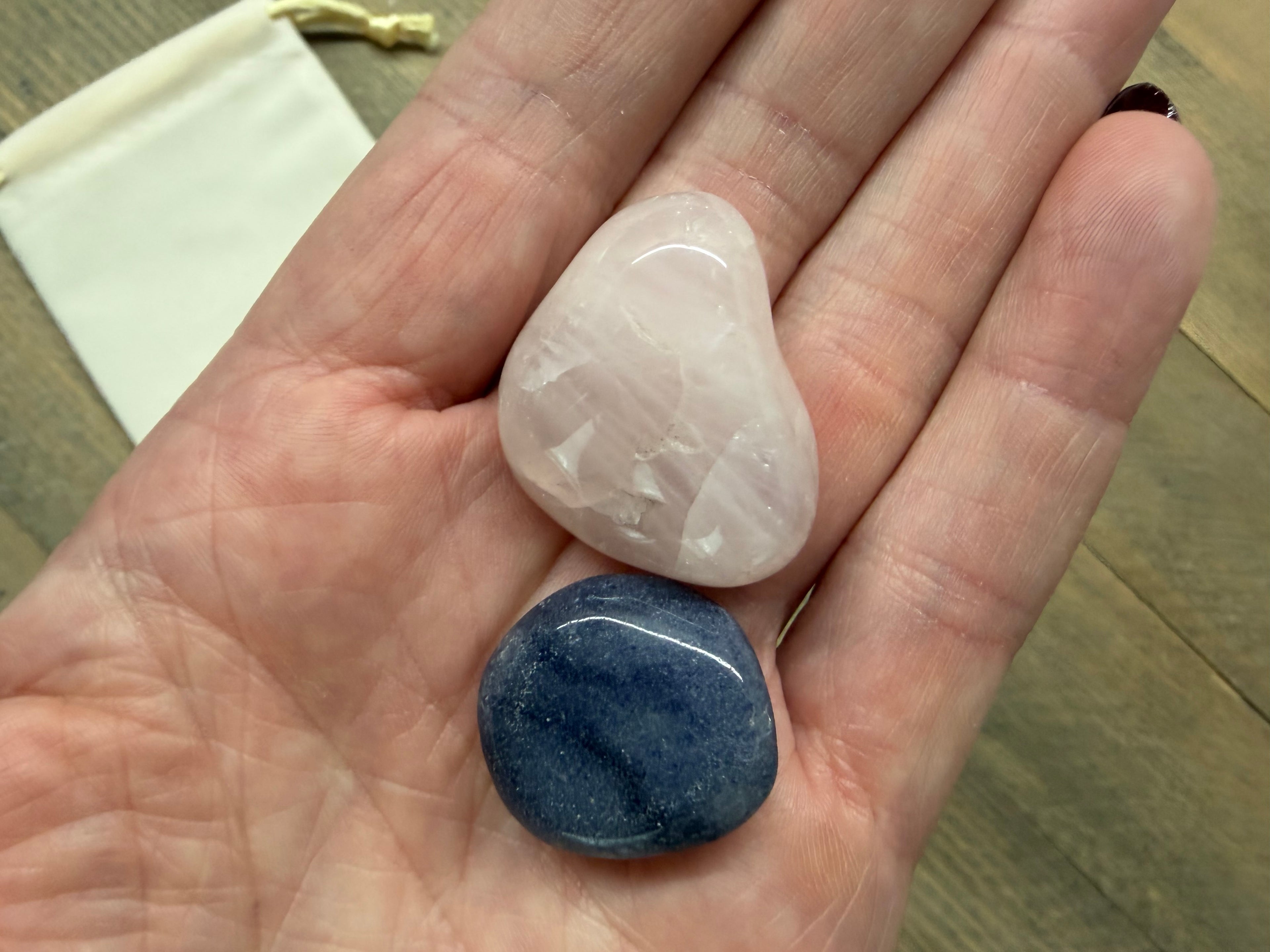 Two stones, one pink and one blue, held in a hand on a wooden surface.
