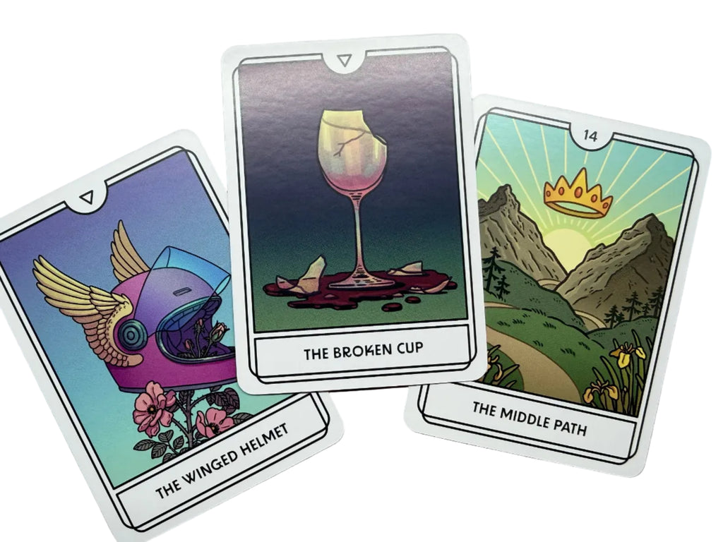 Three tarot cards titled 'The Winged Helmet', 'The Broken Cup', and 'The Middle Path' on a wooden surface.