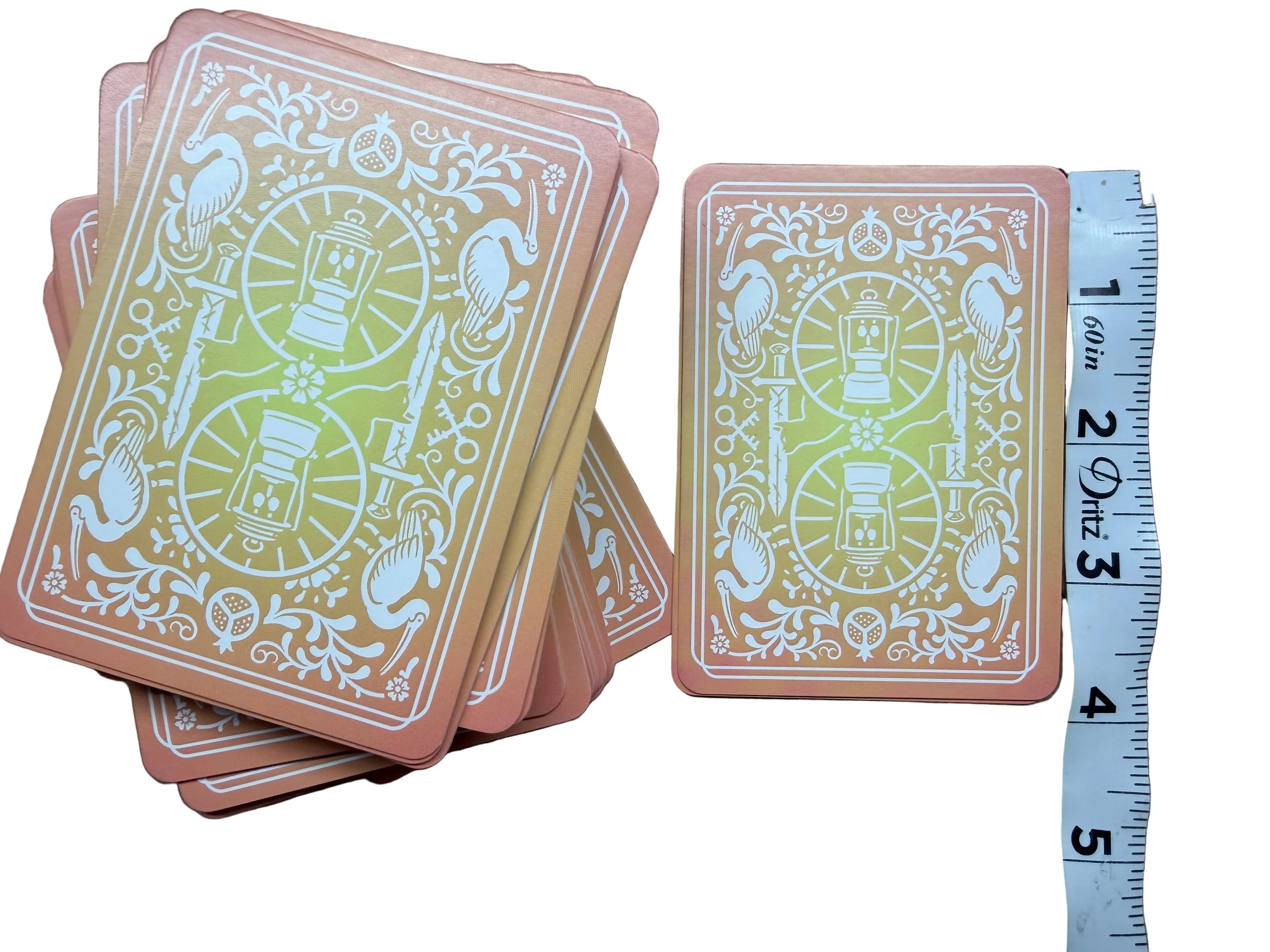 Set of playing cards with decorative design on a wooden surface, accompanied by a ruler for scale.