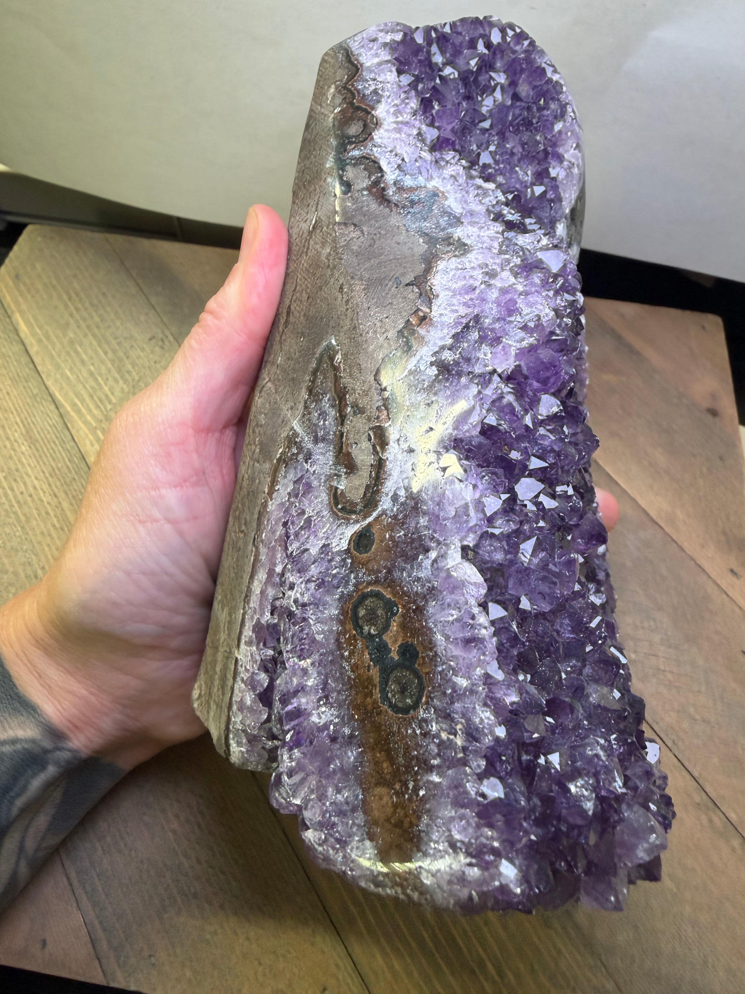 Amethyst crystal held in a hand on a wooden surface