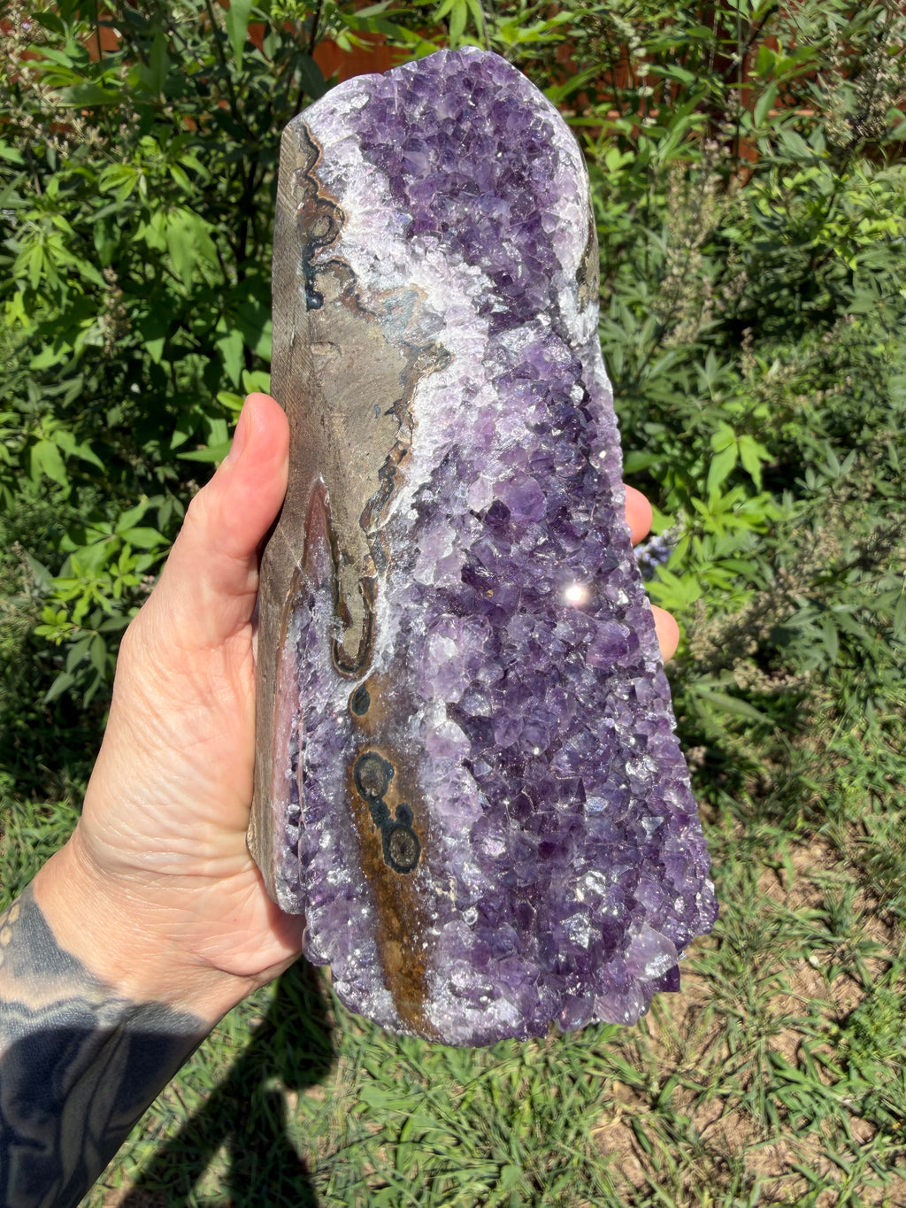 Hand holding a large purple crystal rock against a green outdoor background
