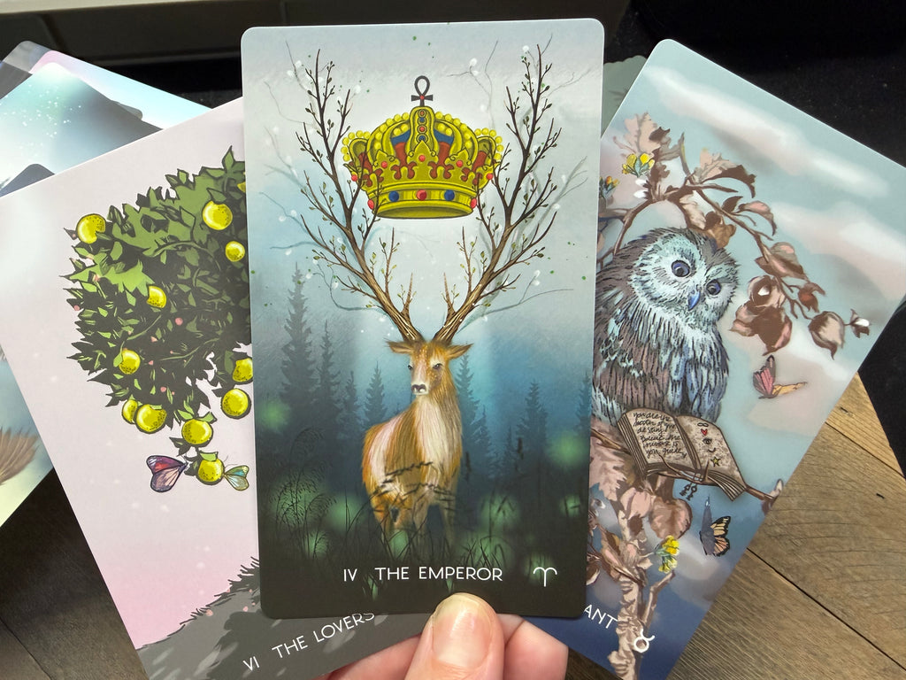 Tarot cards featuring 'The Emperor' card with a deer and crown, held by a hand.