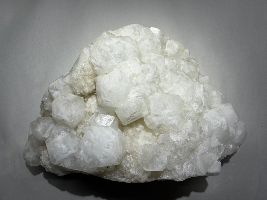 A cluster of white to semi-translucent crystals on a light gray background.