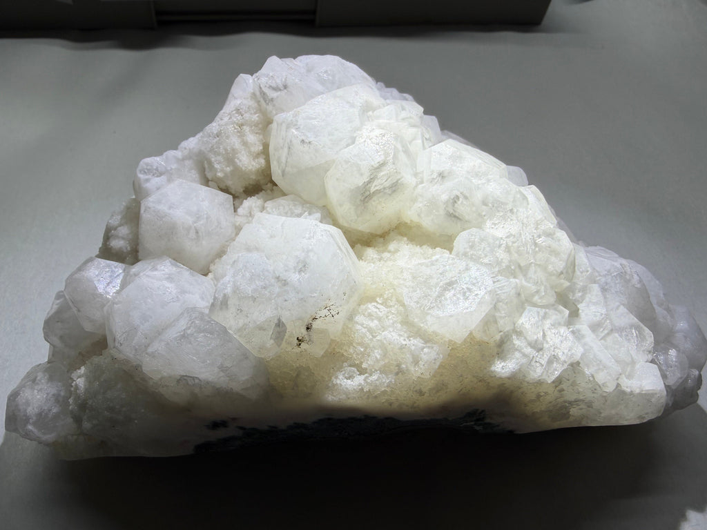 A cluster of rough white to semi-translucent crystals or mineral formations resting on a gray surface.