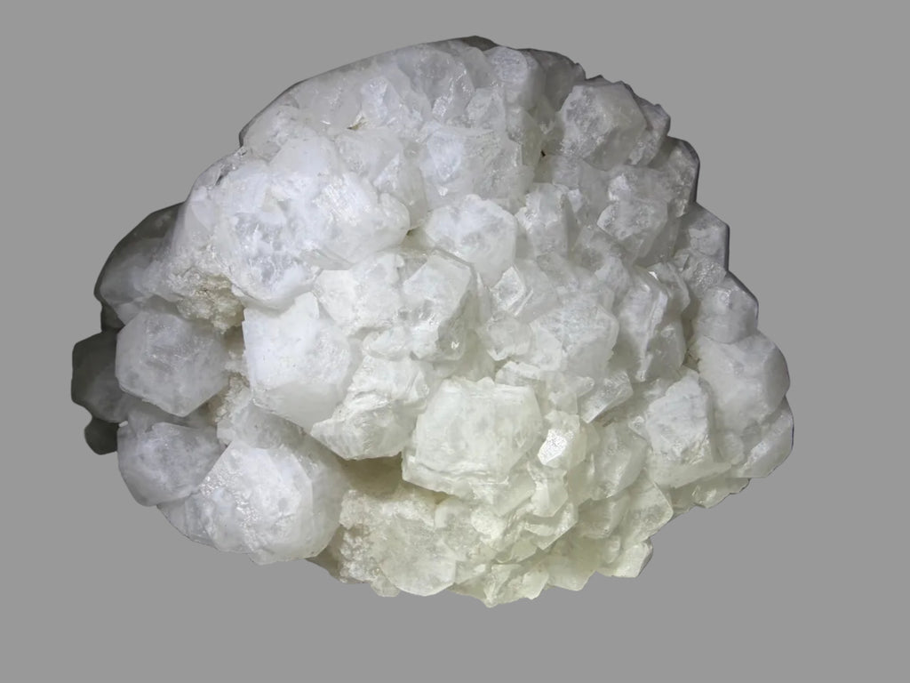 A large cluster of rough white crystals or mineral stones with a bubbly, faceted texture, photographed on a dark surface with a spotlight effect.
