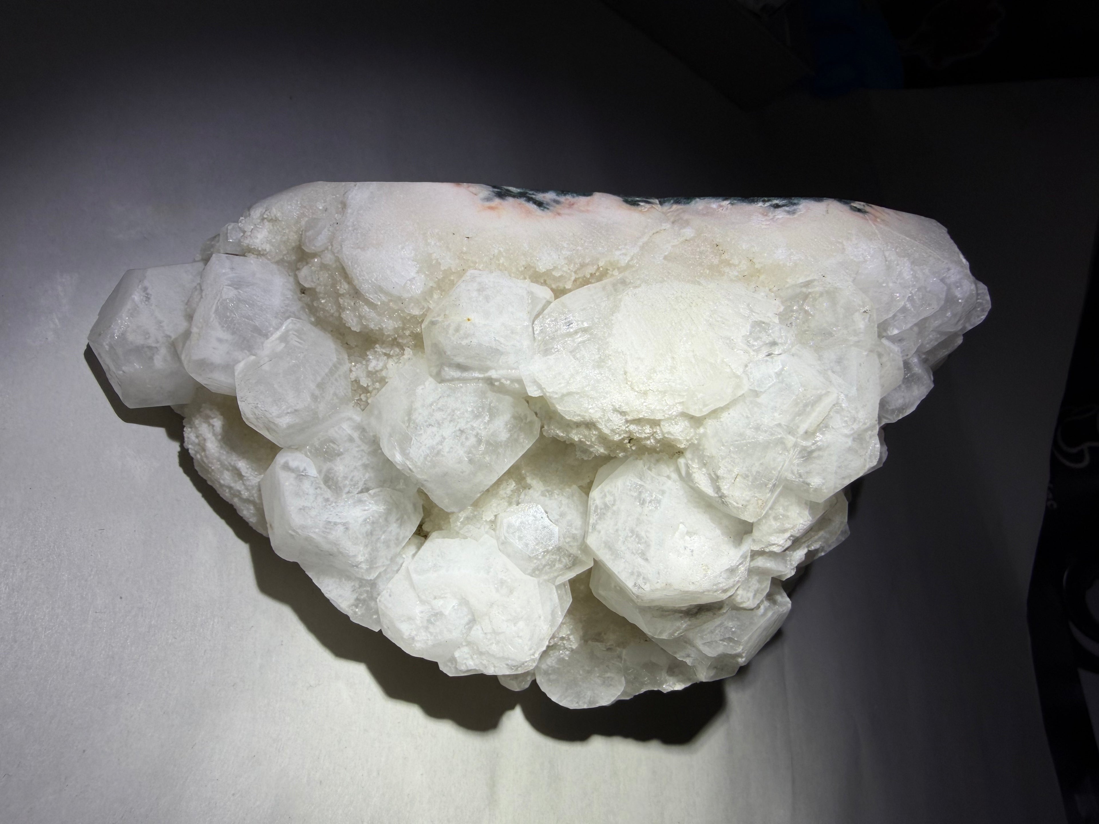 A cluster of rough white crystals or mineral stones photographed on a dark surface against a dark background.