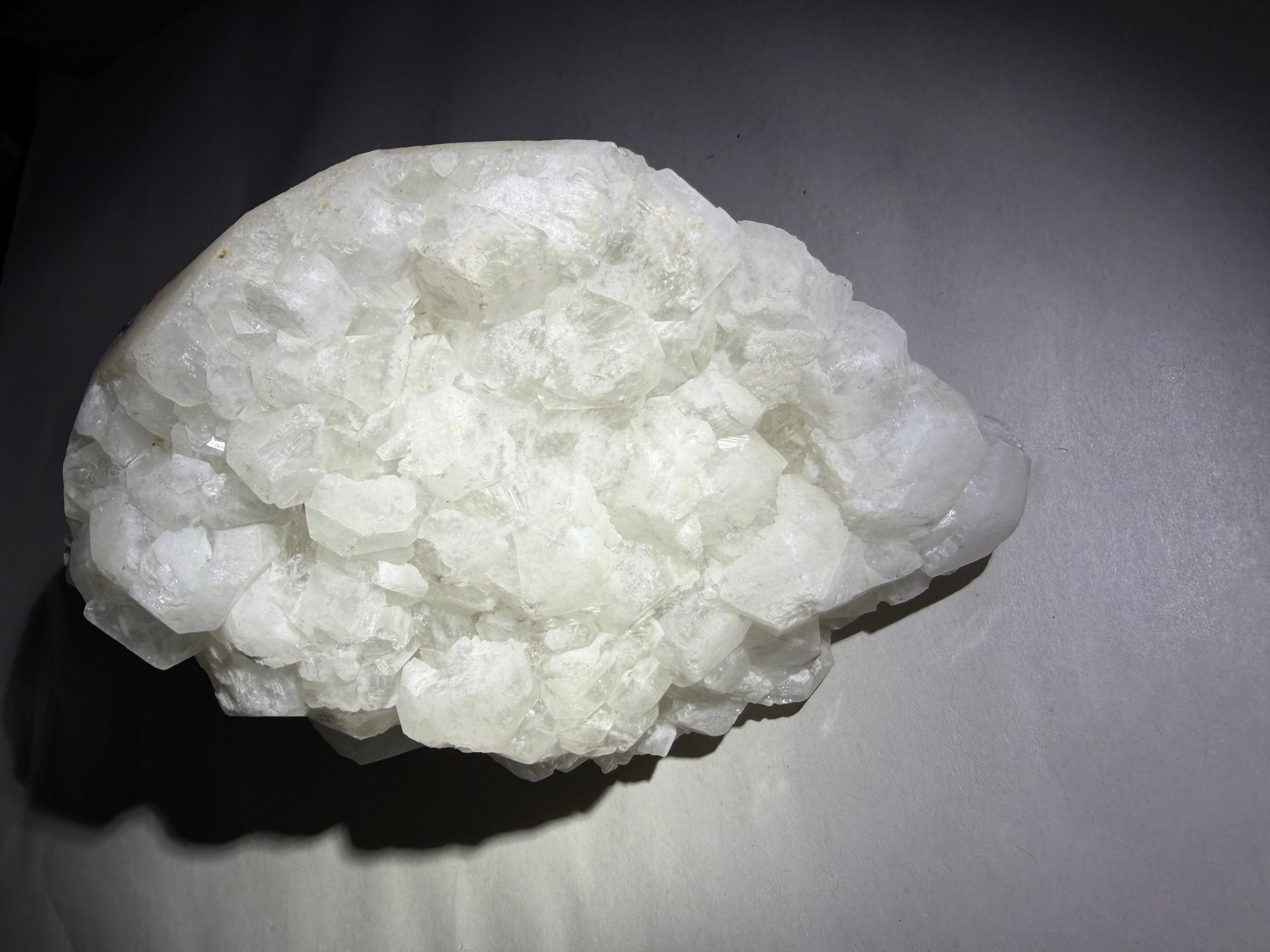 A rough, irregular cluster of white crystalline mineral or gemstone material with a matte to semi-gloss texture, photographed on a dark gray background.