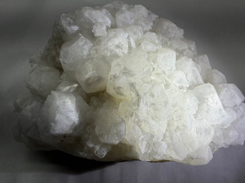 A cluster of rough, translucent white crystals with sharp, jagged edges, resting on a neutral gray surface.