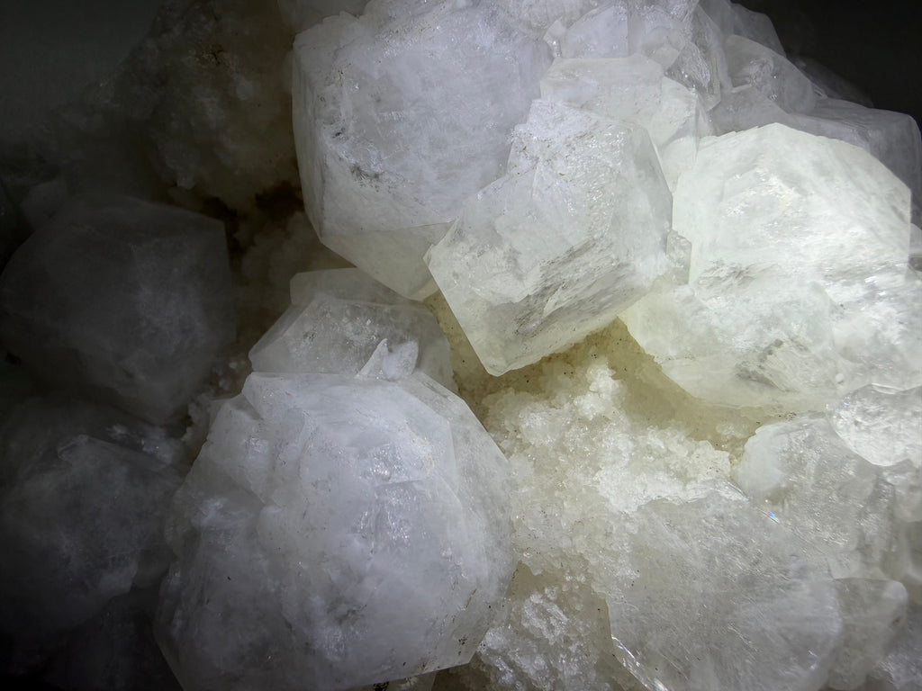 A close-up pile of translucent white and frosted crystal formations with rough, faceted edges, photographed in low light.