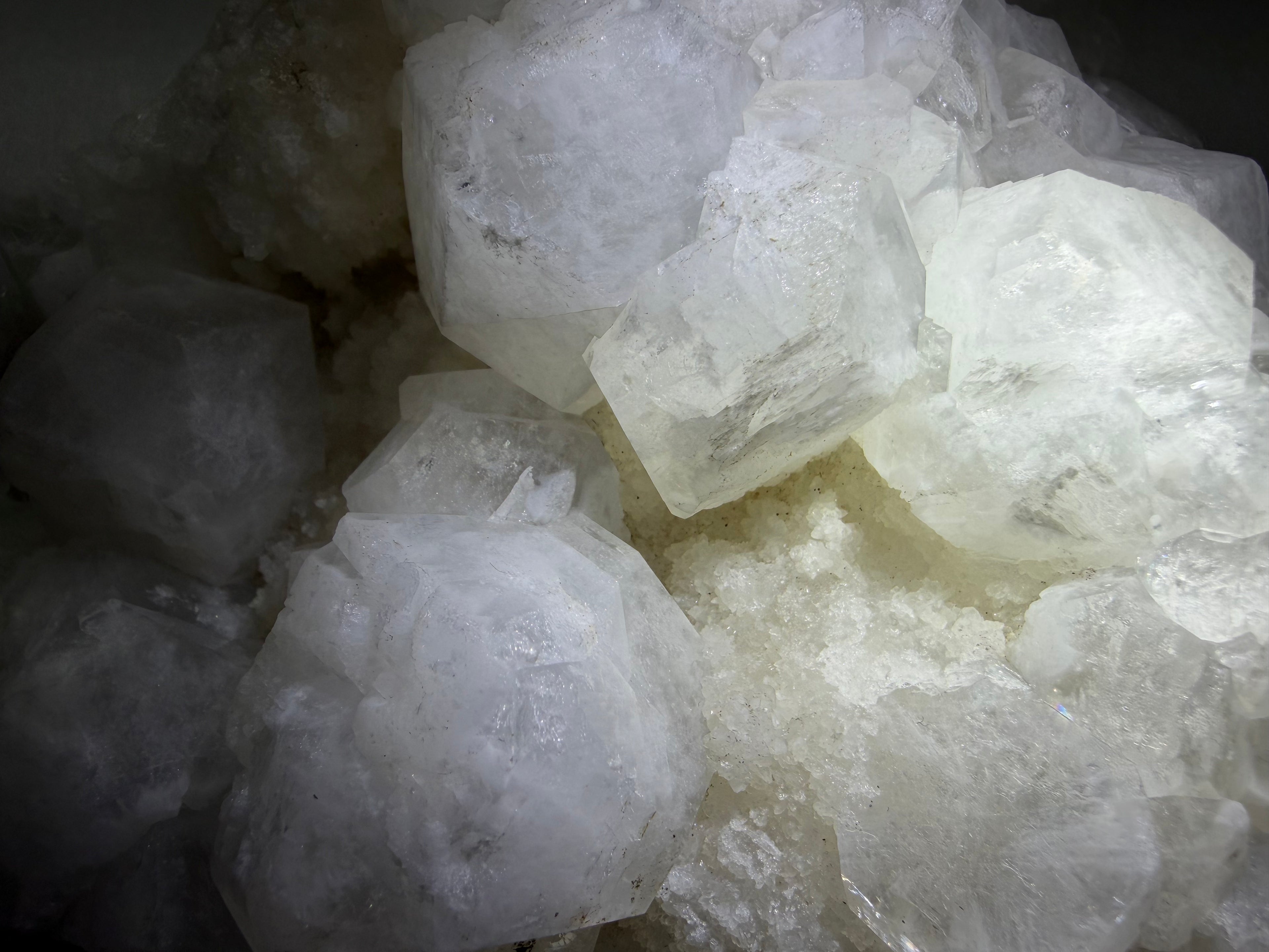 A close-up pile of translucent white and frosted crystal formations with rough, faceted edges, photographed in low light.