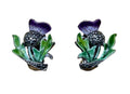 A pair of vintage-style floral enamel pins shaped like purple thistles with green leaves, displayed on a light wood grain background.