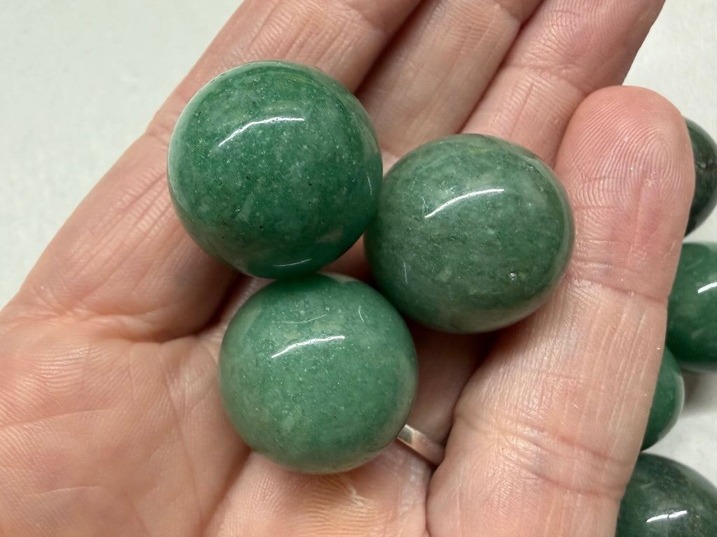Three polished green stone beads held in a person's hand, with additional similar beads visible along the edges.