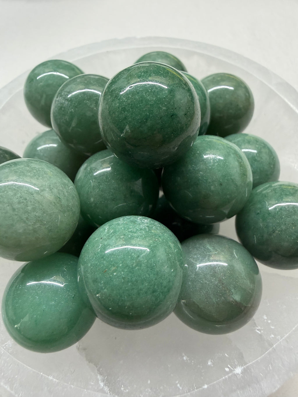 A pile of polished green stone spheres, likely jade or similar material, arranged in a clear plastic container against a white background.