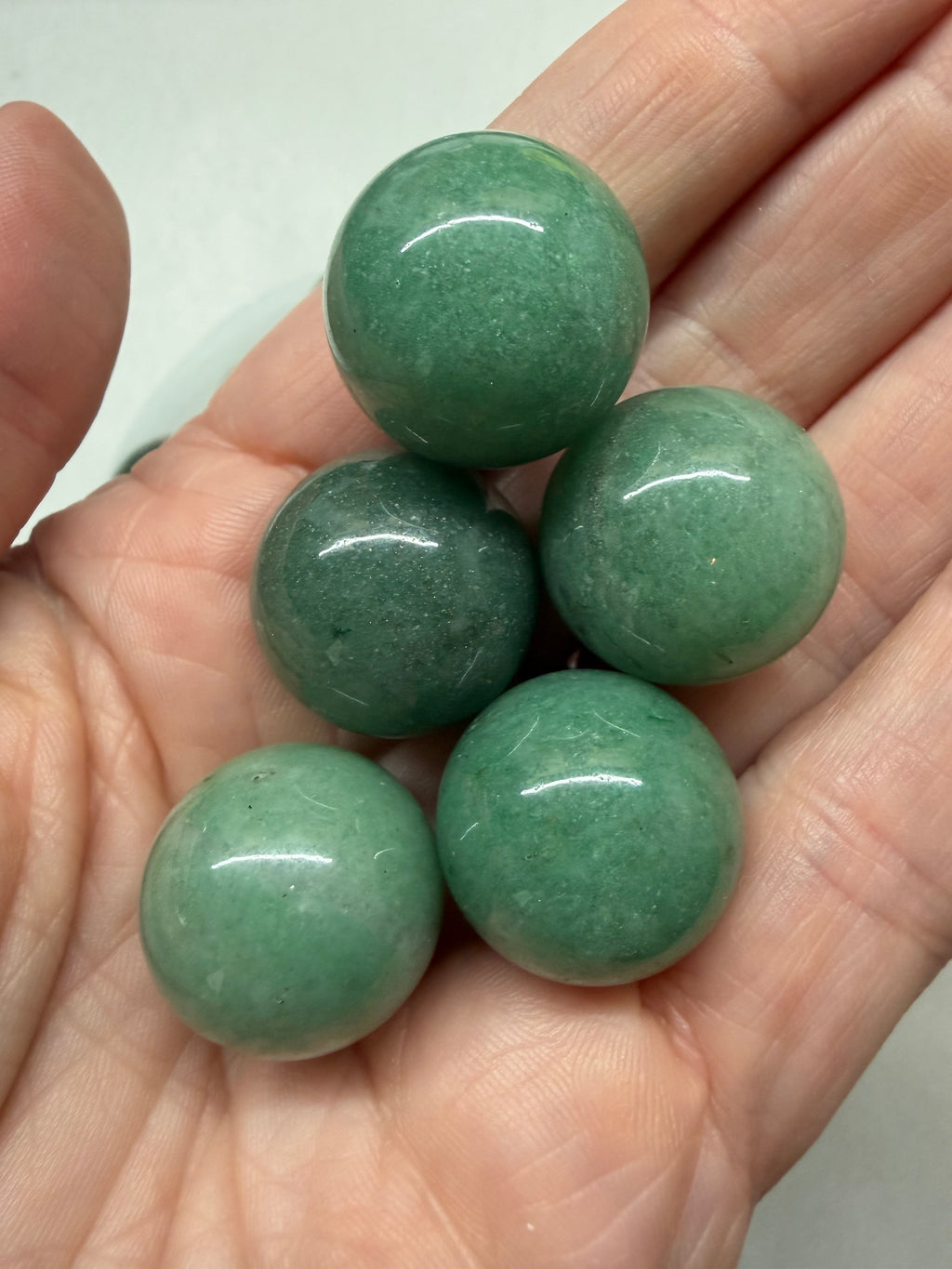 Five polished green stone beads held in a person's hand, photographed close-up against a light neutral background.