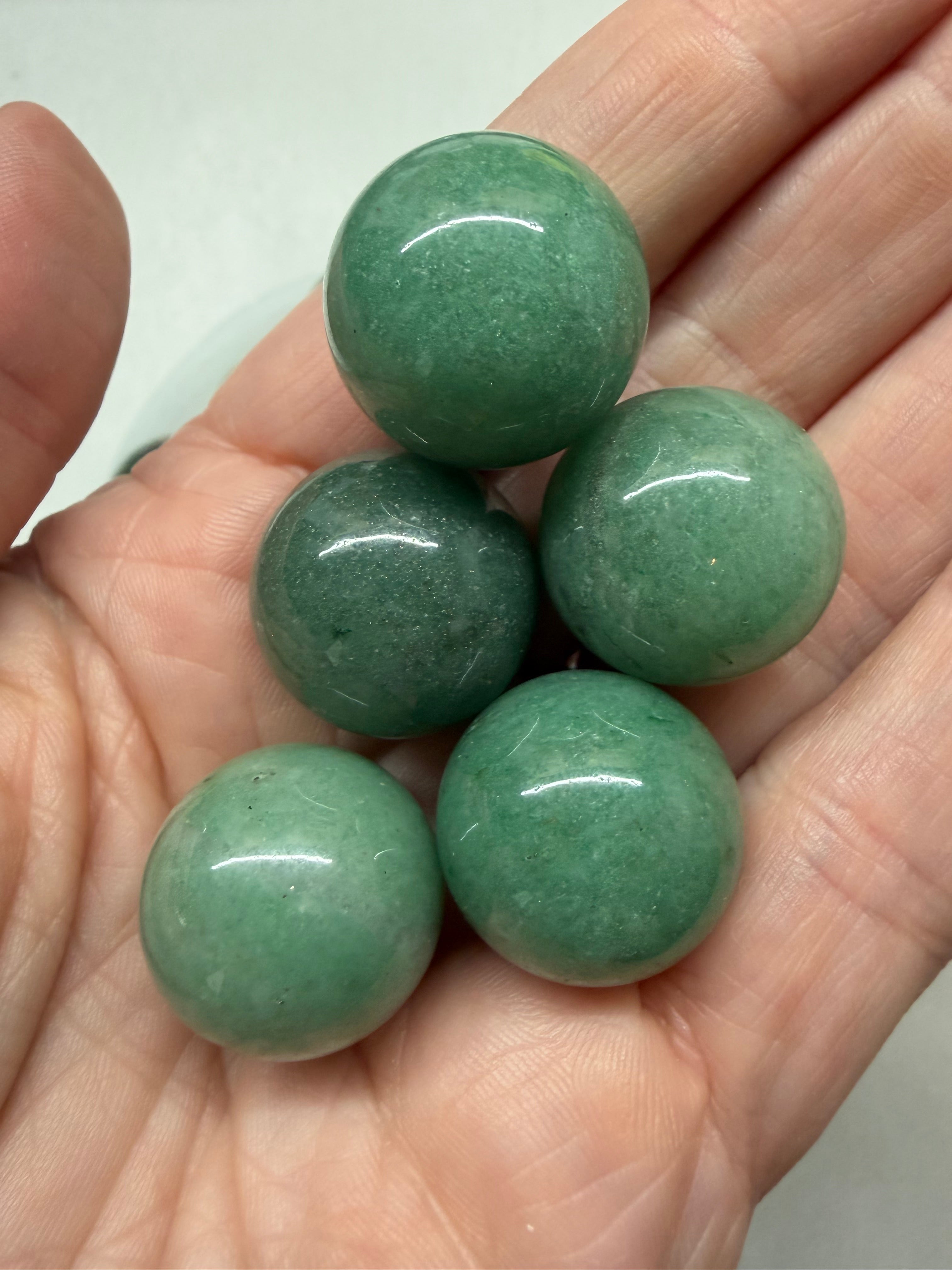 Five polished green stone beads held in a person's hand, photographed close-up against a light neutral background.