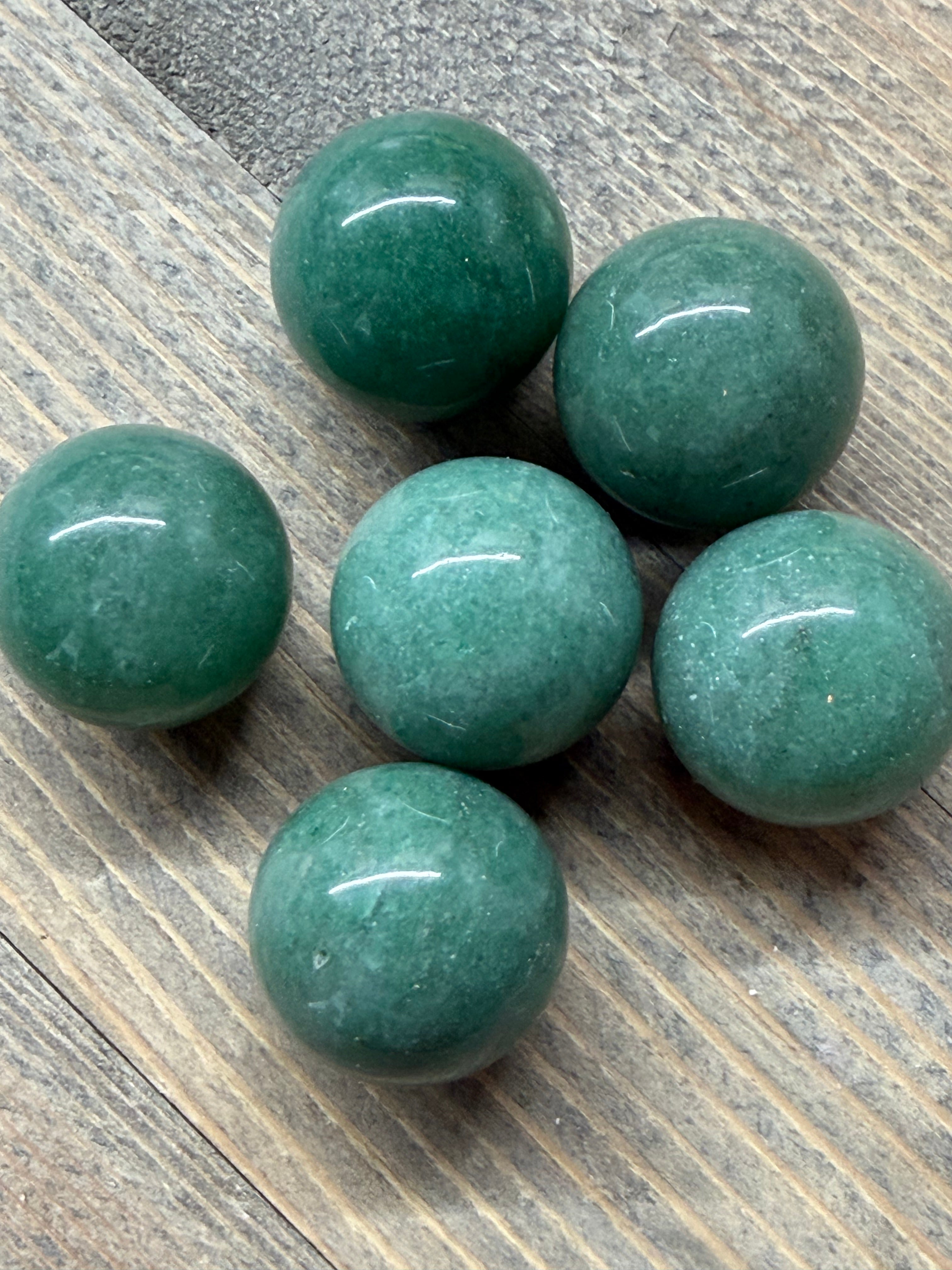 Six polished green stone spheres arranged on a rustic wood surface.