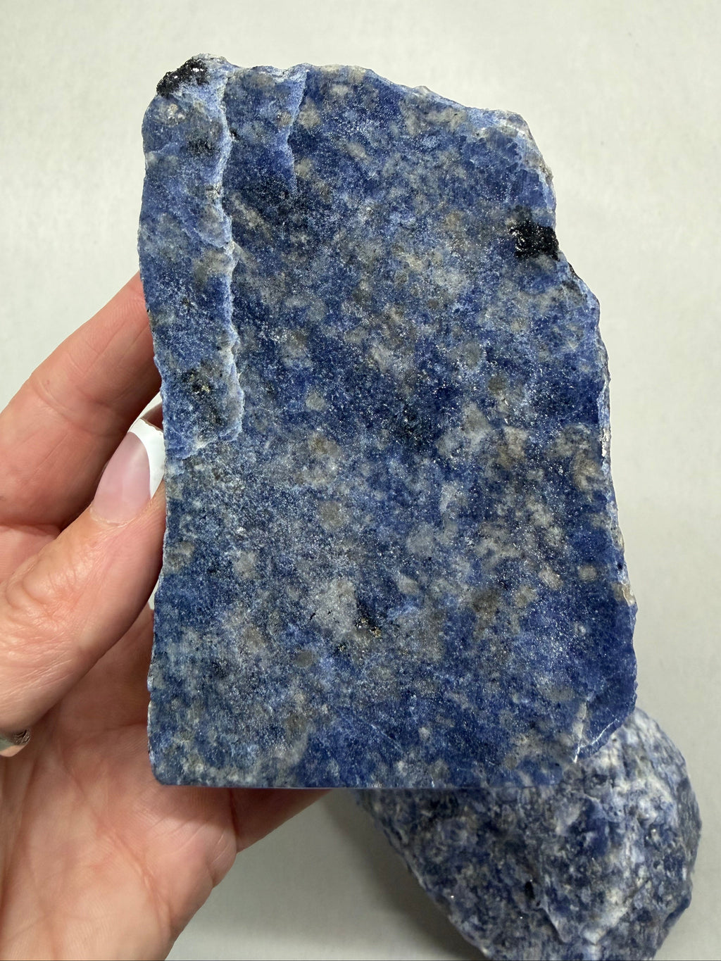 A hand holding a rough blue speckled stone or mineral sample against a plain light background.