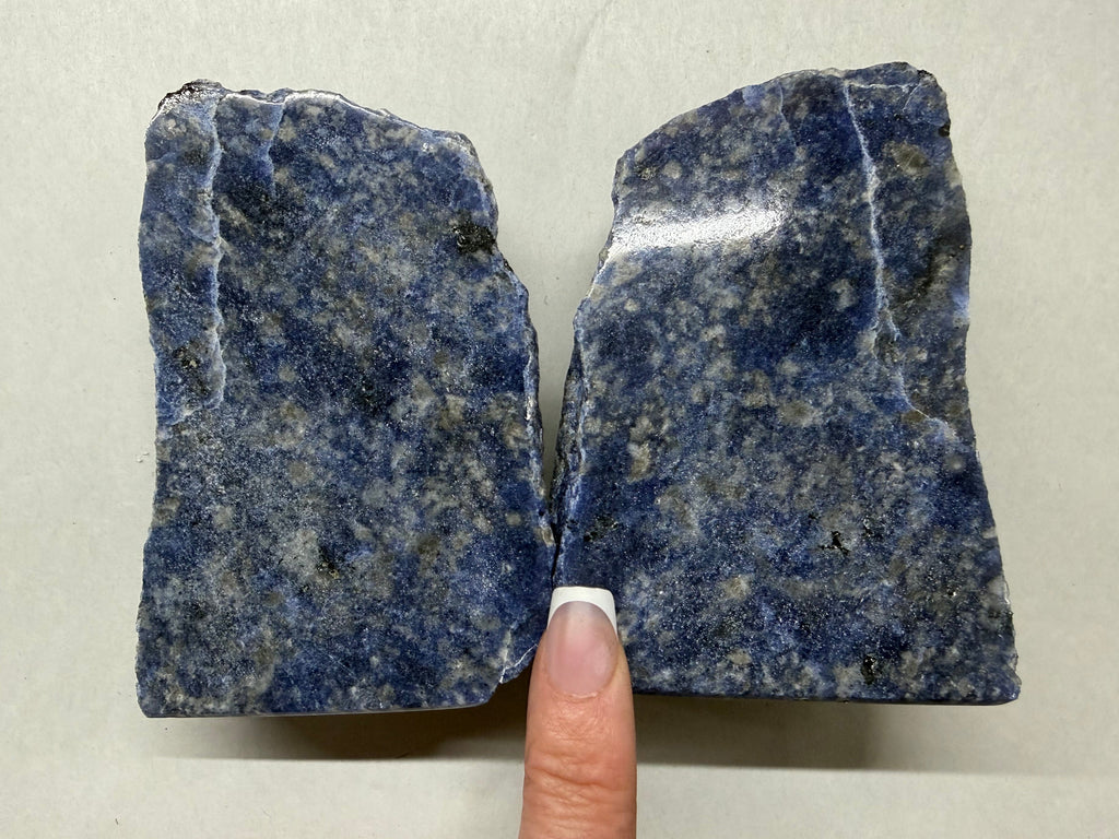 Two rough blue-gray stone slabs held side by side, with a person's finger visible between them for scale, against a plain light background.