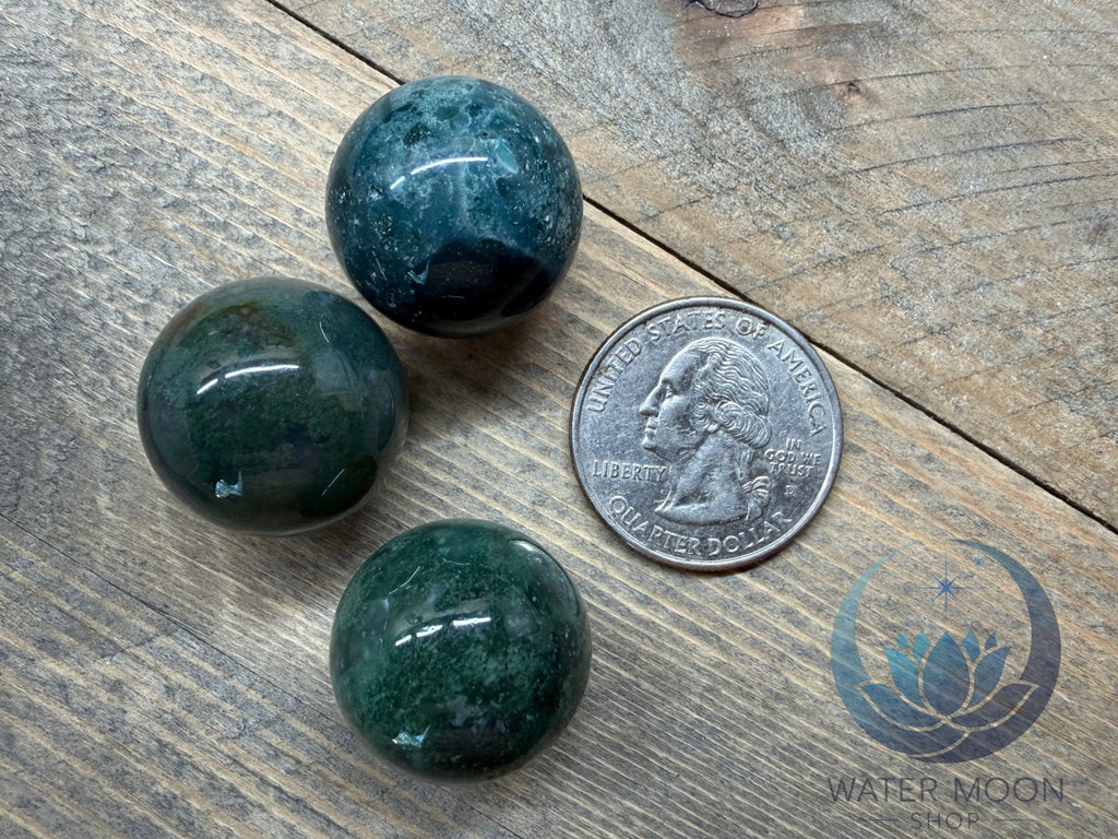 Three green marbles on a wooden surface with a coin for scale.