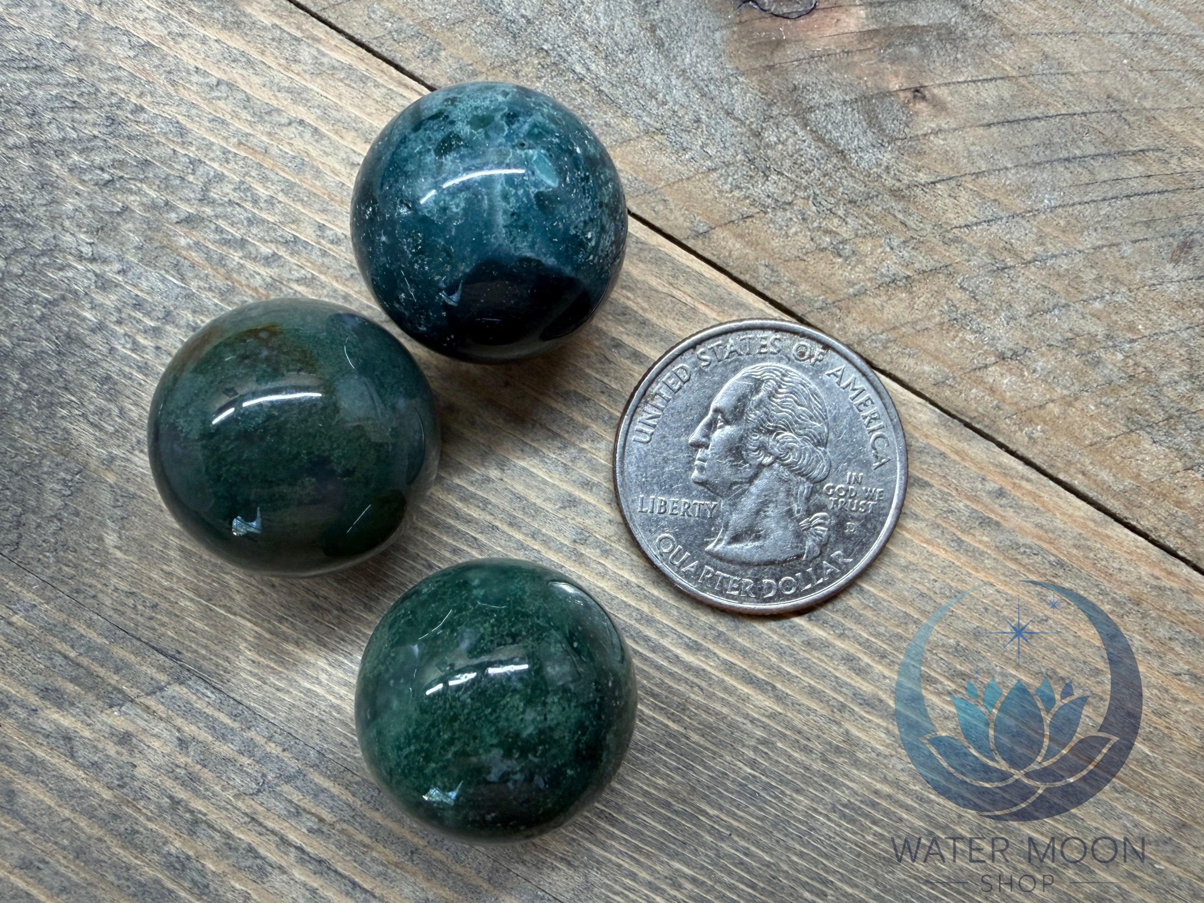 Three green marbles on a wooden surface with a coin for scale.