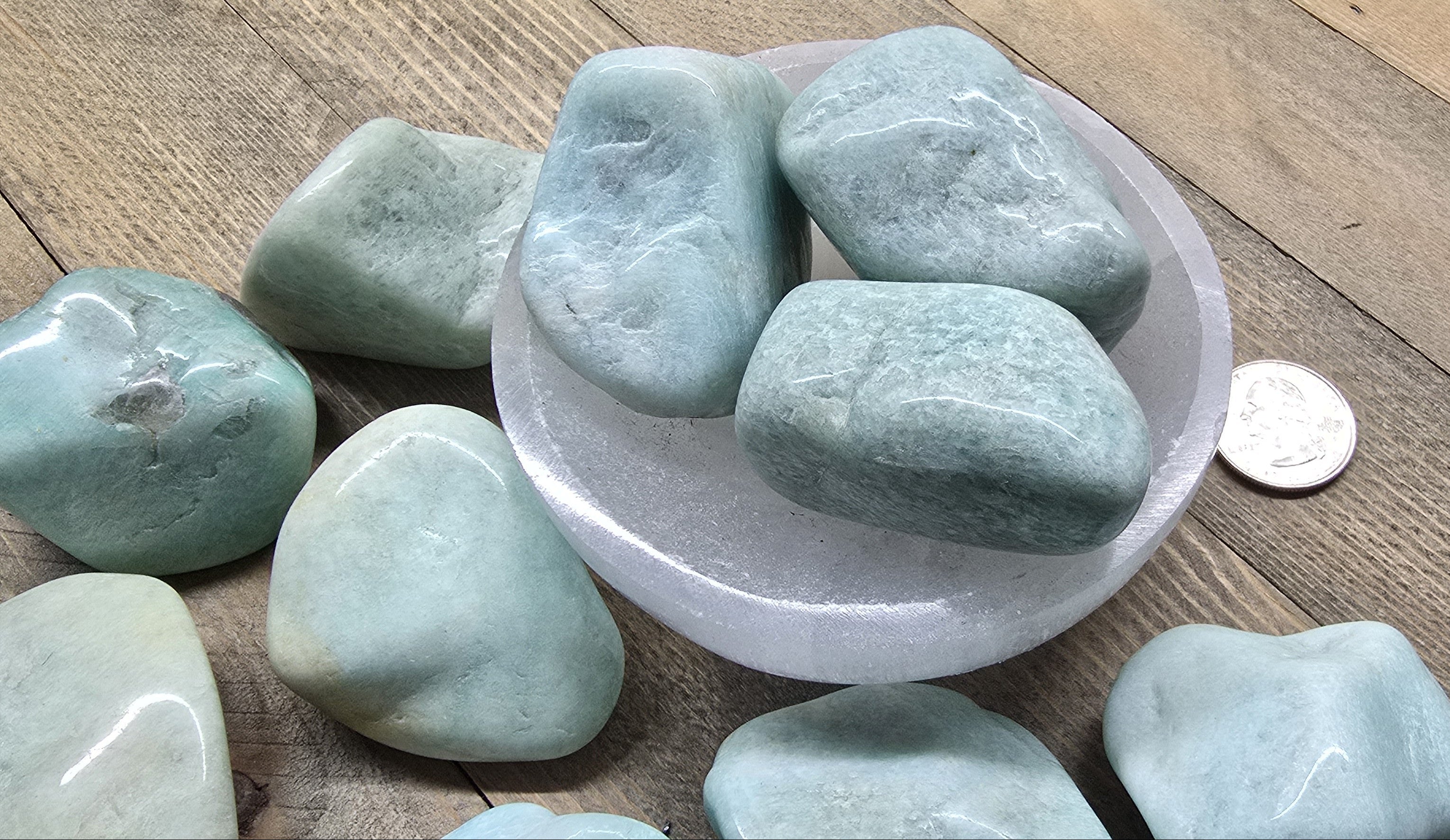 Green stones in a white bowl on a wooden surface with a coin for scale.