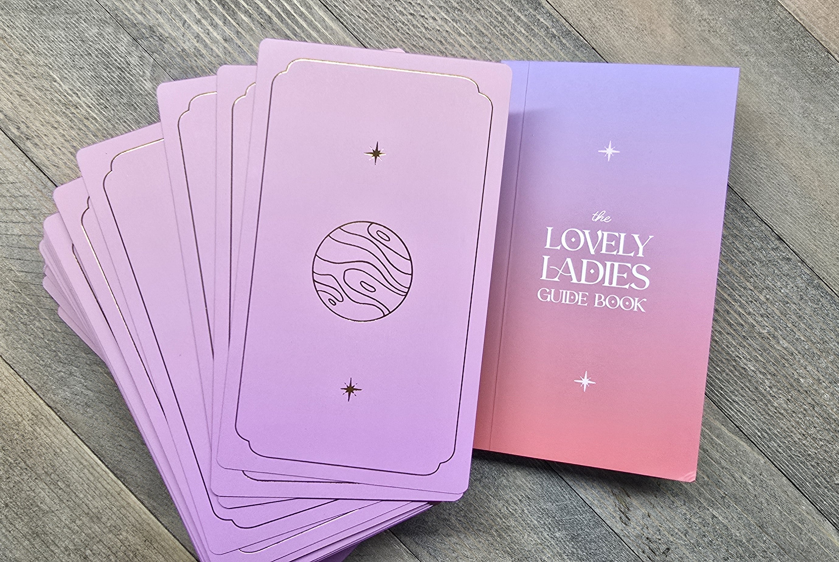 Purple cards with star designs and 'The Lovely Ladies Guide Book' on a wooden surface