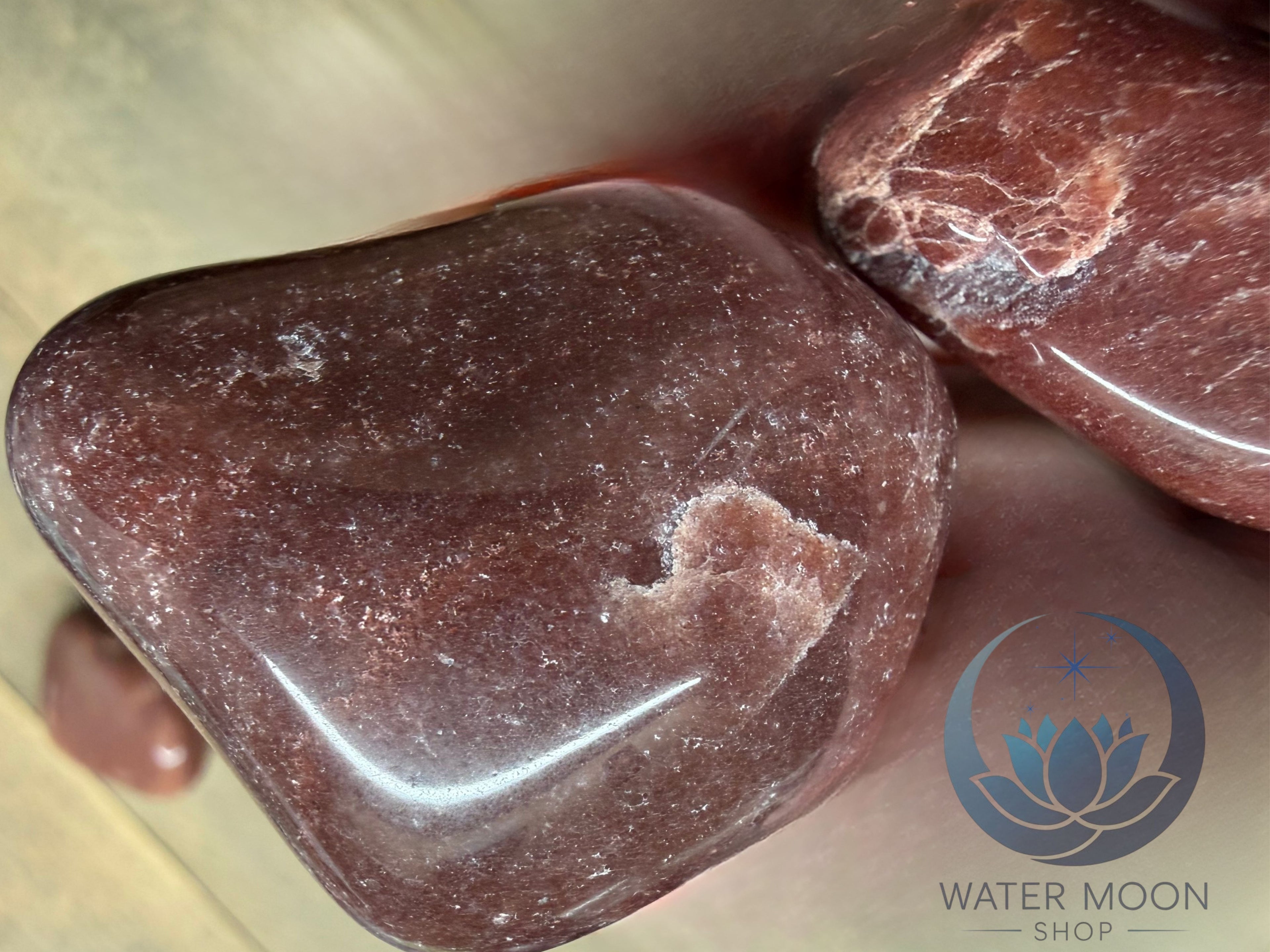 Polished red stone on a light wooden surface with 'Water Moon Shop' logo.