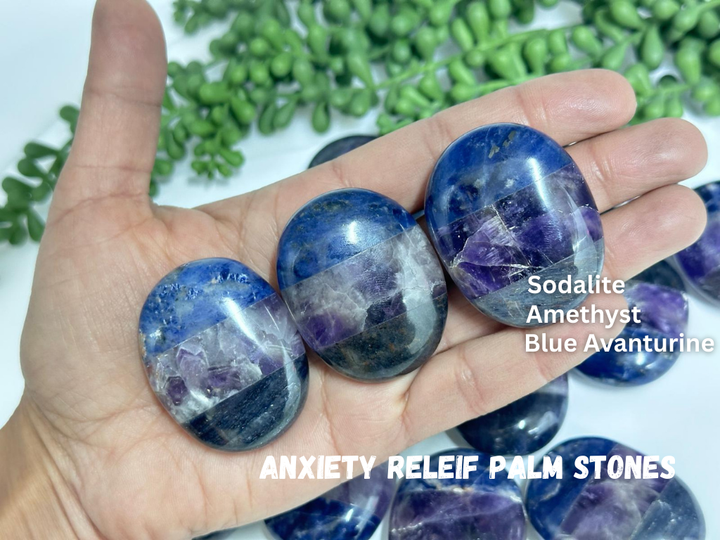 Hand holding three crystal stones labeled Sodalite, Amethyst, and Blue Avanturine with a blurred green plant background.